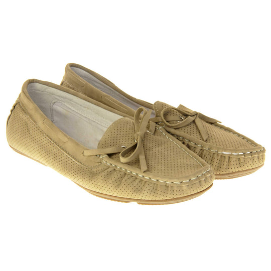 Women's deck shoes. Loafer style boat shoes with a beige faux leather upper and tiny dot cut-outs. Beige lace detail running around the outside of the collar. White stitching detailing around the top of the shoe. Cream leather lining and beige sole. Both feet together at a slight angle.