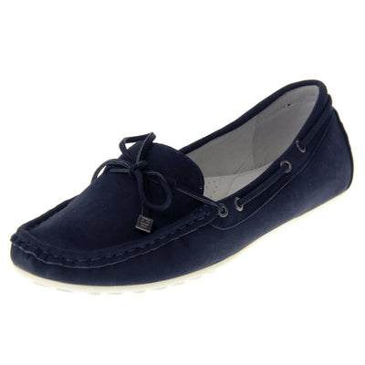 Women's deck shoes. Moccasin style boat shoes with a navy blue faux suede upper. Stitching detail around the top and a lace and bow detail around the collar and tongue of the shoe. Grey leather lining and thin white sole. Left foot at an angle.