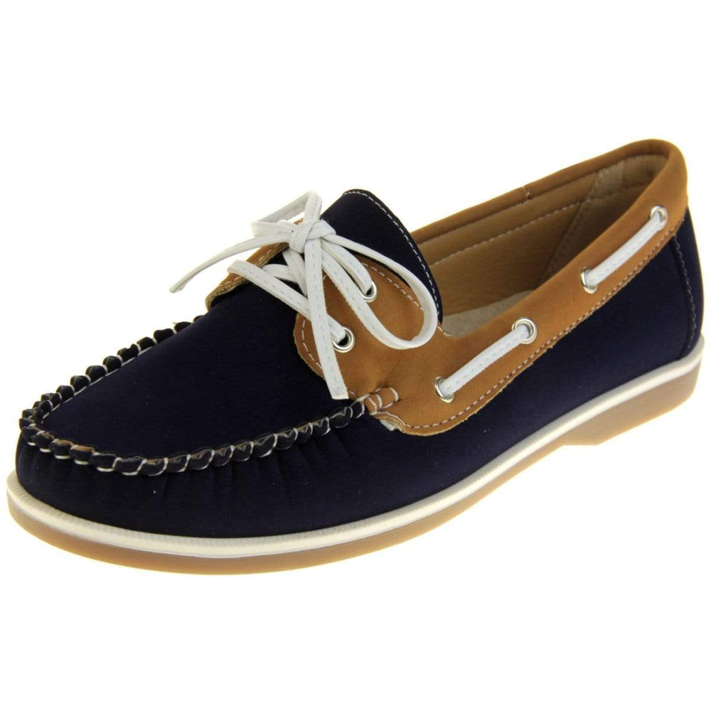Womens Deck Shoes - Navy blue and tan brown faux leather upper with white rim around the tan sole. Leather effect cord strips with eyelets detailing down the side of the shoe with lace up fastening to the front. Left angle facing.