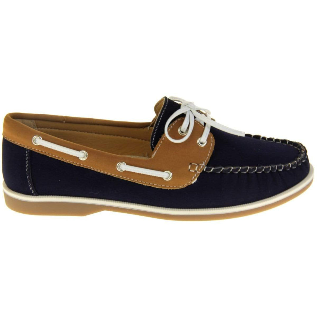 Womens Deck Shoes - Navy blue and tan brown faux leather upper with white rim around the tan sole. Leather effect cord strips with eyelets detailing down the side of the shoe with lace up fastening to the front. Side facing.