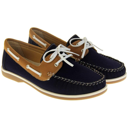 Womens Deck Shoes - Navy blue and tan brown faux leather upper with white rim around the tan sole. Leather effect cord strips with eyelets detailing down the side of the shoe with lace up fastening to the front. Both feet at an angle.