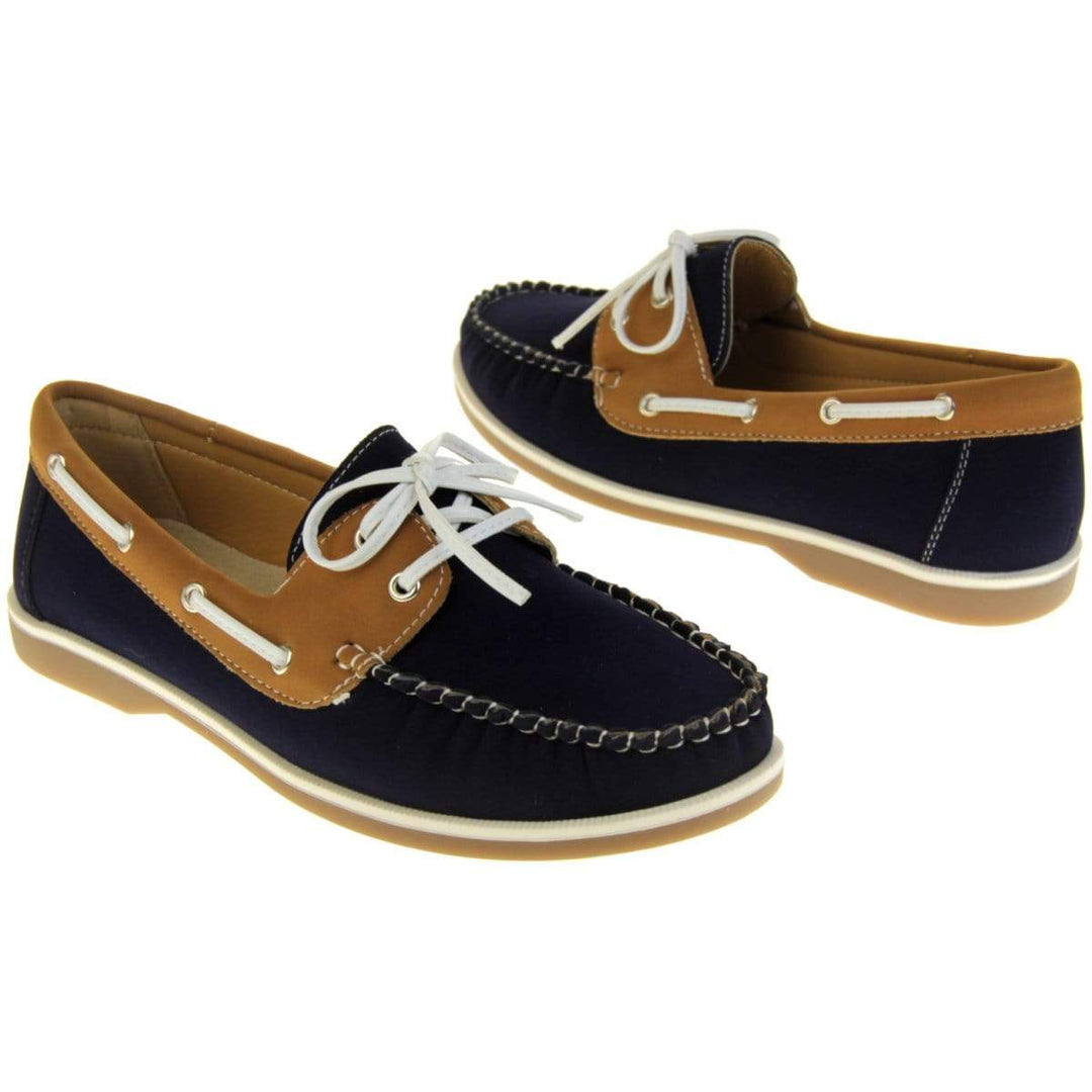 Womens Deck Shoes - Navy blue and tan brown faux leather upper with white rim around the tan sole. Leather effect cord strips with eyelets detailing down the side of the shoe with lace up fastening to the front. One foot facing the front, other foot facing the rear.
