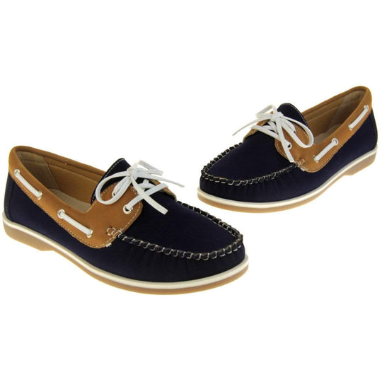 Womens Deck Shoes - Navy blue and tan brown faux leather upper with white rim around the tan sole. Leather effect cord strips with eyelets detailing down the side of the shoe with lace up fastening to the front. Both feet at different angles.