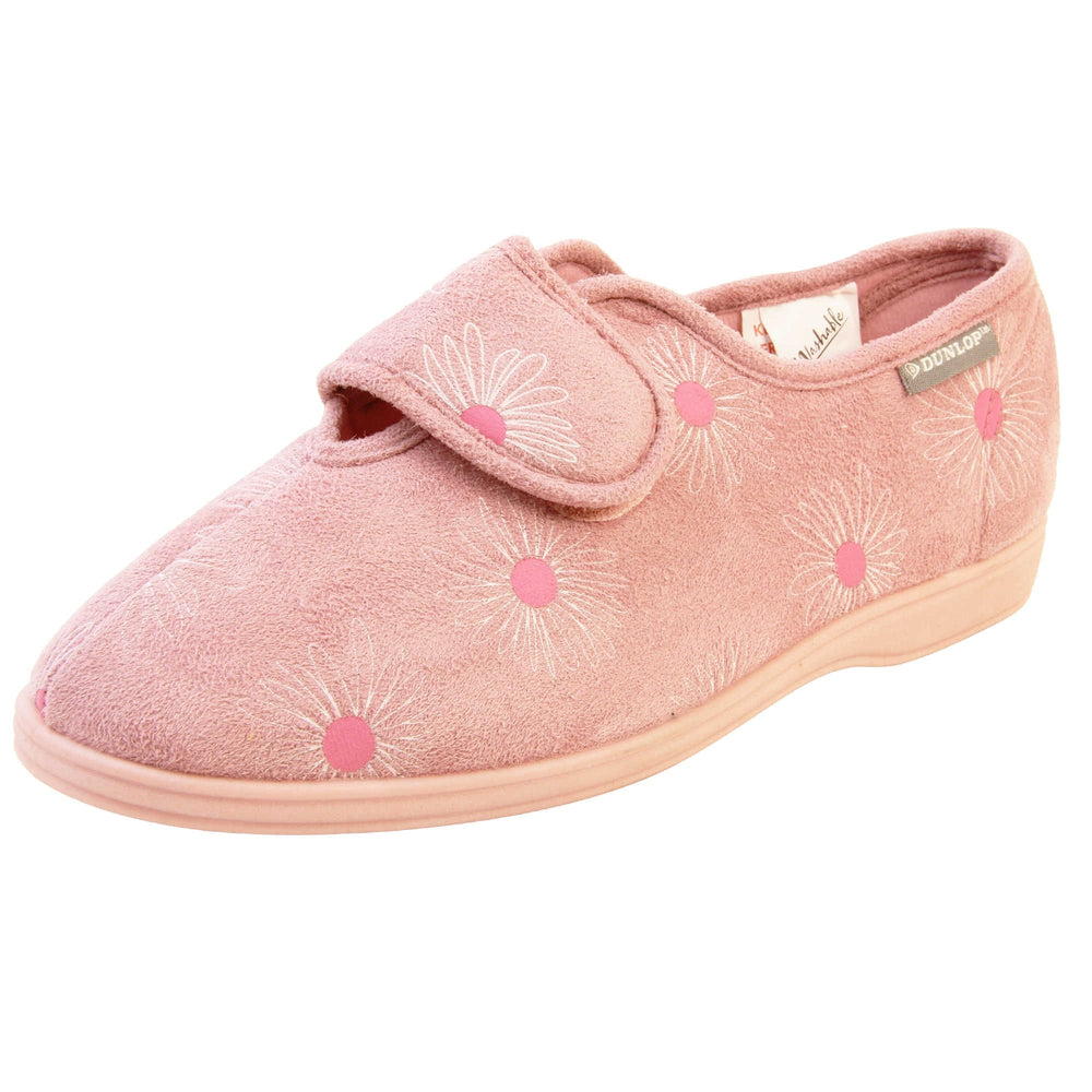 Pink flower slippers. Womens full back slipper. With a pale pink upper with white daisy design with bright pink for the middle of the flowers. Touch fasten strap over the top of the foot to adjust the fit. Pink textile lining and firm pink sole. Left foot at an angle.