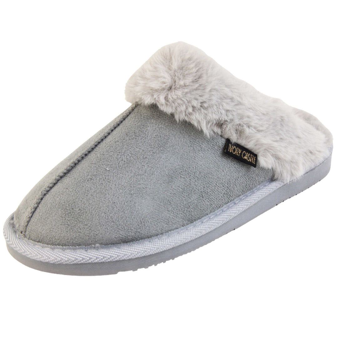Womens faux fur mule slippers. Slip on style slippers with light grey faux suede uppers. Light grey faux fur lining and collar. Firm grey outsole with grip on the bottom. Left foot at an angle.