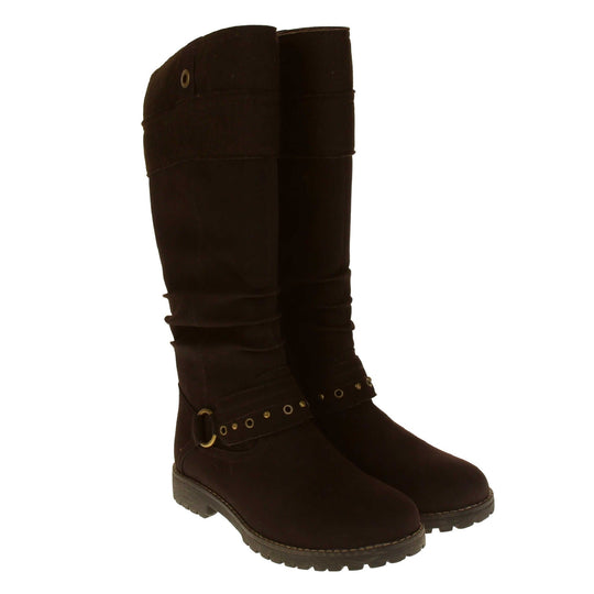 Womens faux suede knee high boot. Tall boots with a dark brown faux nubuck leather upper with a felt decorative cuff around the top. A strap with stud embellishment goes around the front of the ankle connected by a gold loop. Stitching detail around the outsole and the ankle. Full length zip to the inside leg. Both feet together from an angle.