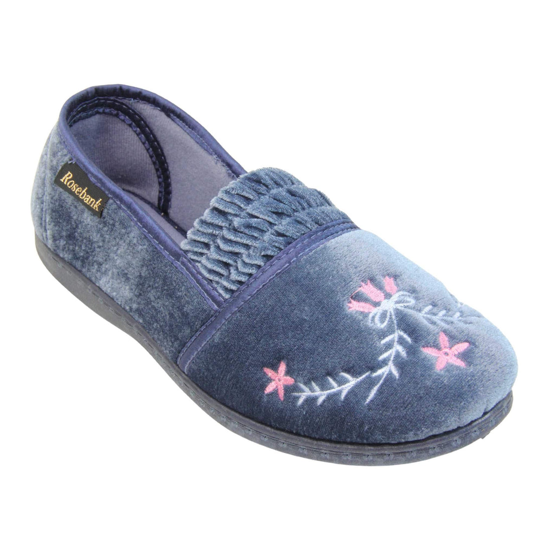 Womens full slippers. Full back slippers in a loafer style. With light blue velour uppers and an embroidered pale blue and pink flower detail. Ruched velour elasticated gusset. Blue textile lining and piping around the collar. Blue firm sole. Right foot at an angle.
