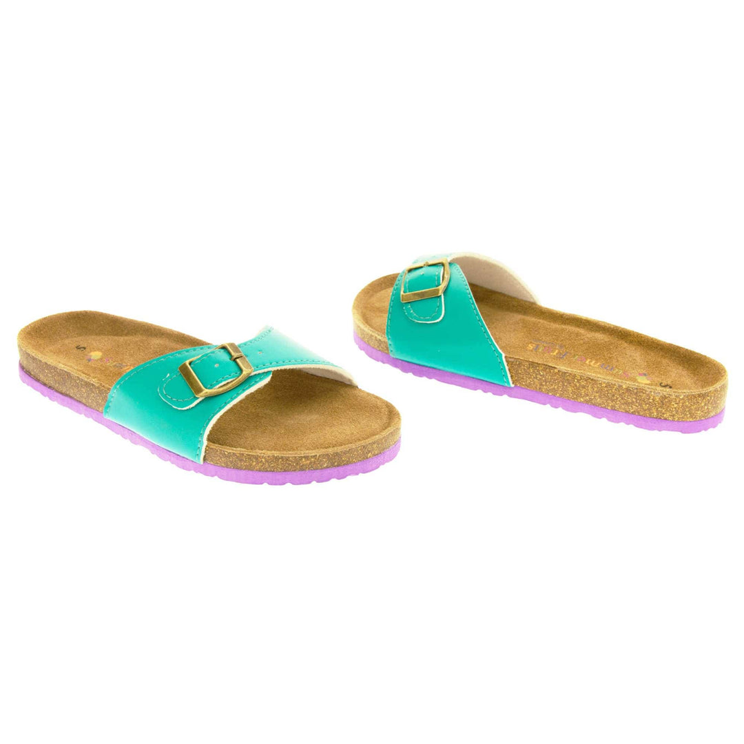 Womens green sliders. Green faux leather strap with gold buckle. Soft tan faux suede footbed with cork effect outsole and purple sole. Both feet at an angle facing top to tail.