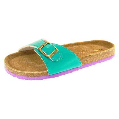 Womens green sliders. Green faux leather strap with gold buckle. Soft tan faux suede footbed with cork effect outsole and purple sole. Left foot at an angle.