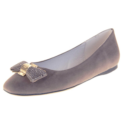 Women's grey flats. Ballet style shoes with a grey faux suede upper. Grey bow detail to the top with diamantes covering it and a gold coloured metal loop round the middle. Cream leather lining and black sole. Left foot at an angle.
