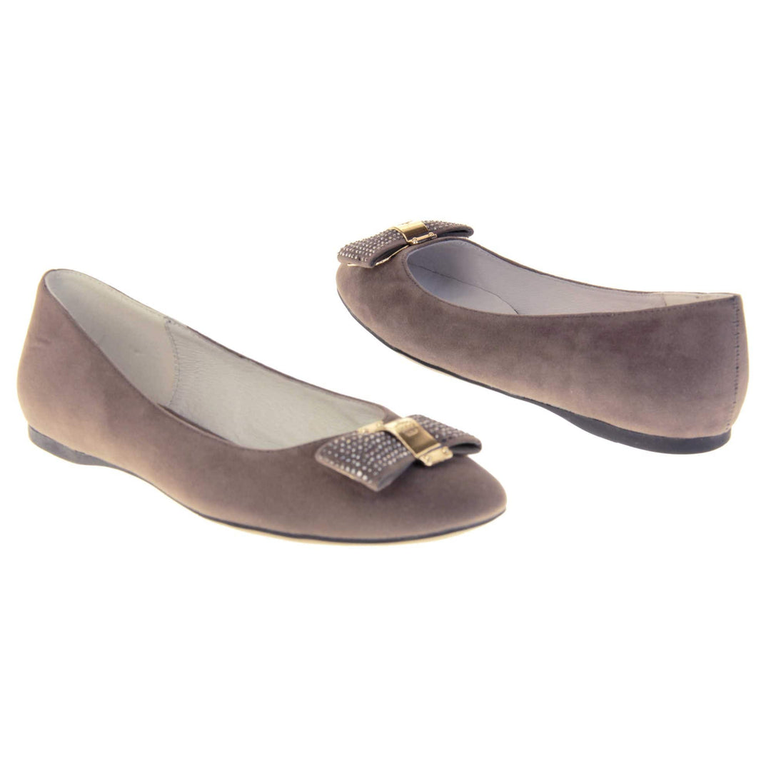 Women's grey flats. Ballet style shoes with a grey faux suede upper. Grey bow detail to the top with diamantes covering it and a gold coloured metal loop round the middle. Cream leather lining and black sole. Both feet at an angle facing top to tail.
