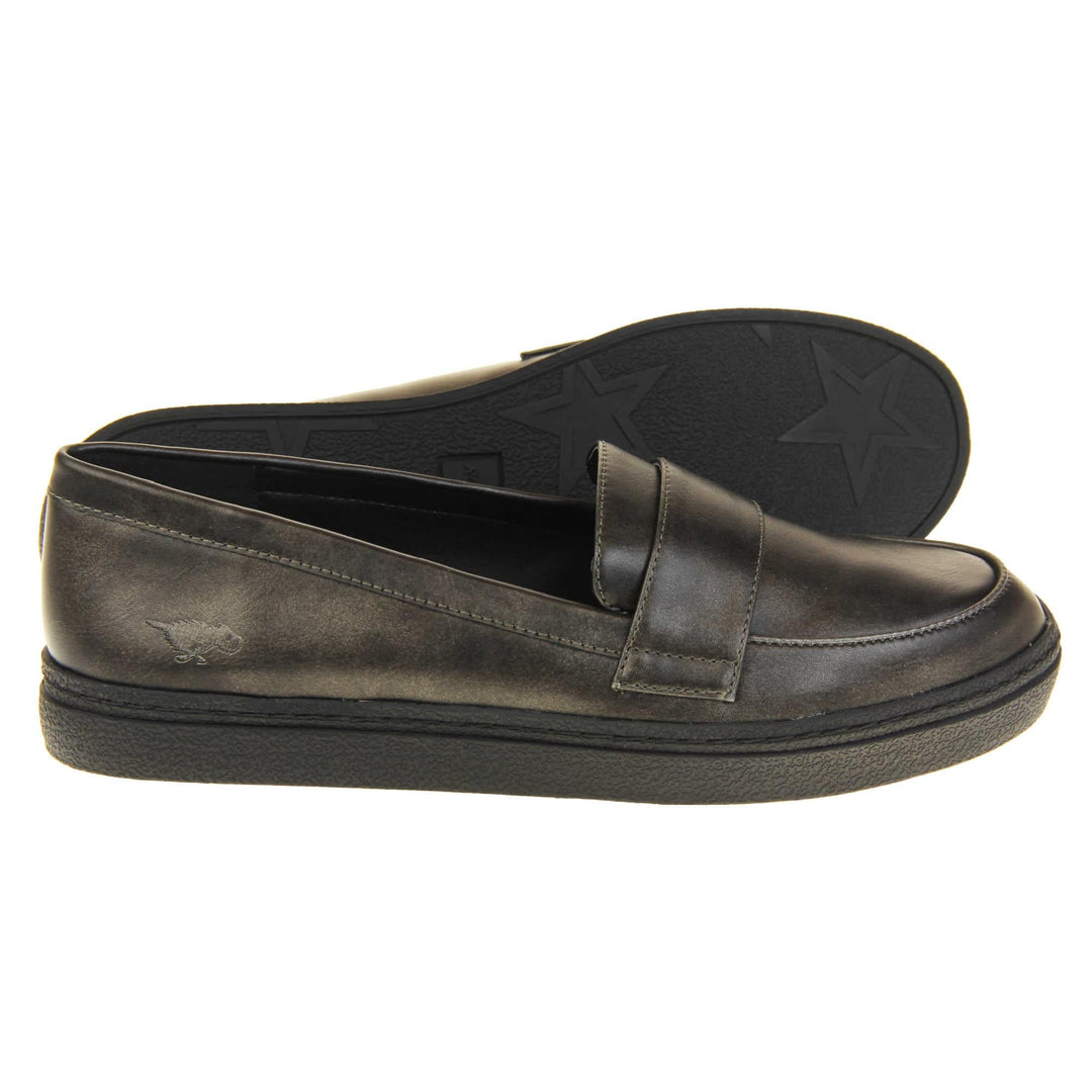 Women's grey loafer. Loafer style shoes with a pewter grey faux leather upper. With a bar detail over the foot. Rocket Dog logo to the outside heel. Chunky black sole with slip resistant grip to the bottom.  Both feet from a side profile with the left foot on its side behind the the right foot to show the sole.