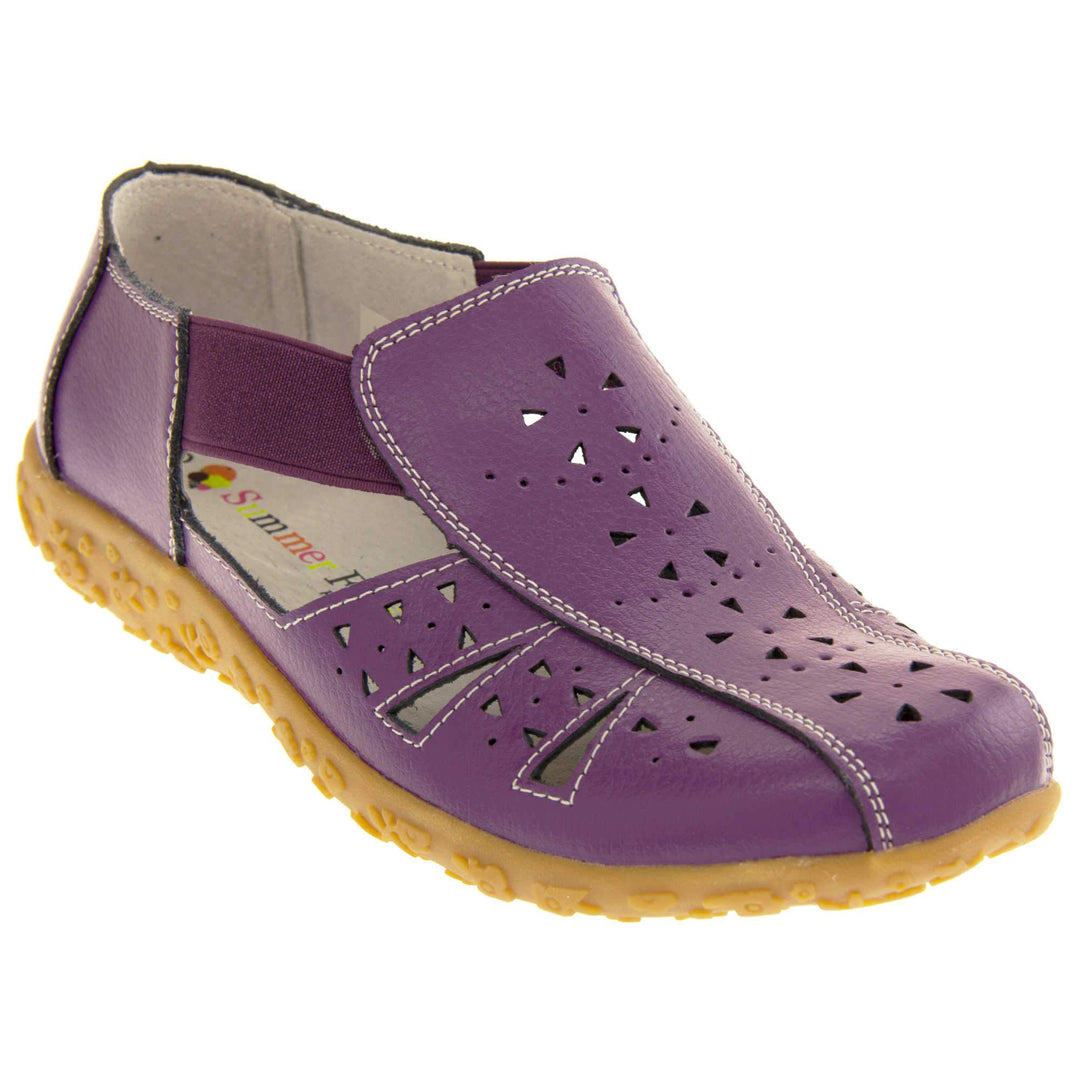 Womens leather sandals. Purple leather closed toe sandals with white stitched detailing. With small cut out details on the upper. Purple elasticated strips from tongue to ankle to allow more room for a better fit. Cream coloured leather insole and lining. Brown sole with heel having a slight platform with raised flower design for grip. Right foot at an angle.