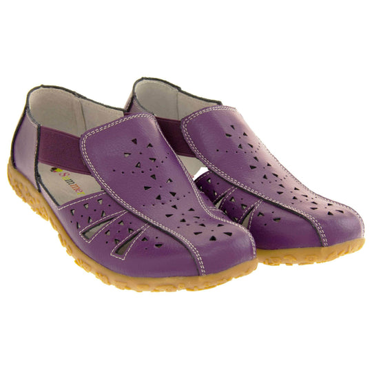 Womens leather sandals. Purple leather closed toe sandals with white stitched detailing. With small cut out details on the upper. Purple elasticated strips from tongue to ankle to allow more room for a better fit. Cream coloured leather insole and lining. Brown sole with heel having a slight platform with raised flower design for grip. Both feet together from an angle.