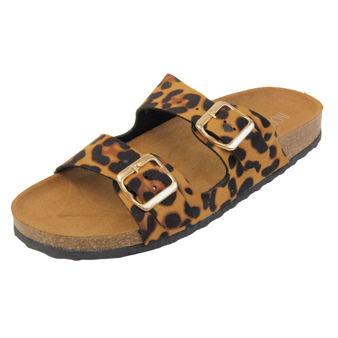 Leopard print sandals. Womens dual strap slip on sandals. With a leopard print synthetic suede upper with a gold buckle on each strap. Brown faux suede insole with a moulded footbed. Cork effect outsole with black base with grip to the bottom. Left foot at an angle.