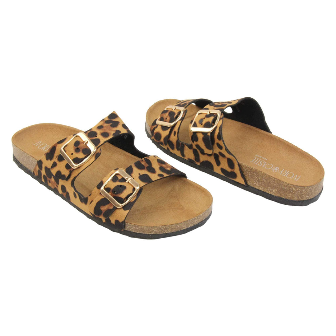 Leopard print sandals. Womens dual strap slip on sandals. With a leopard print synthetic suede upper with a gold buckle on each strap. Brown faux suede insole with a moulded footbed. Cork effect outsole with black base with grip to the bottom. Both feet at an angle facing top to tail.