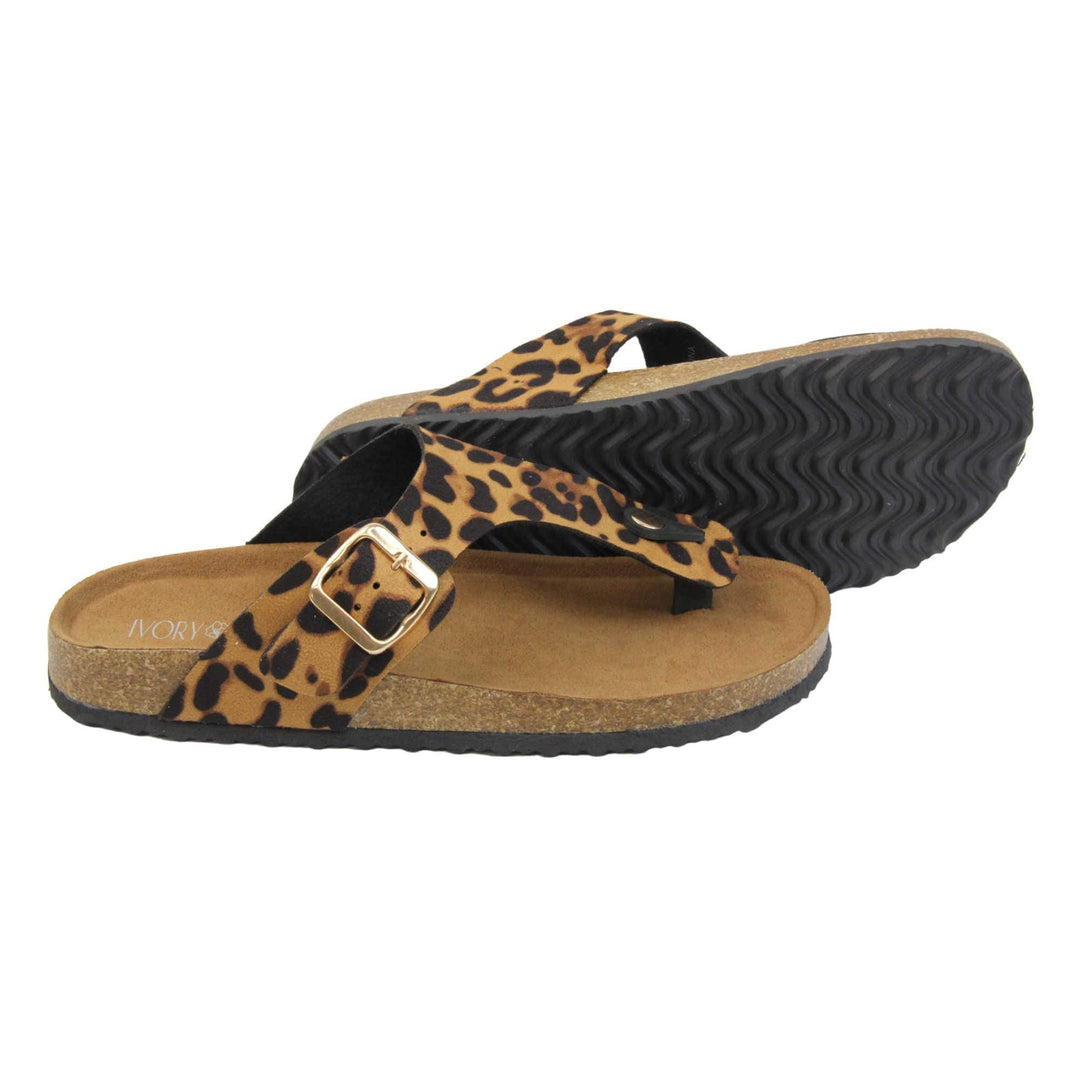 Leopard print sandals. Womens dual strap slip on sandals. With a leopard print synthetic suede upper with a gold buckle on each strap. Brown faux suede insole with a moulded footbed. Cork effect outsole with black base with grip to the bottom. Both feet from a side profile with the left foot on its side behind the the right foot to show the sole.