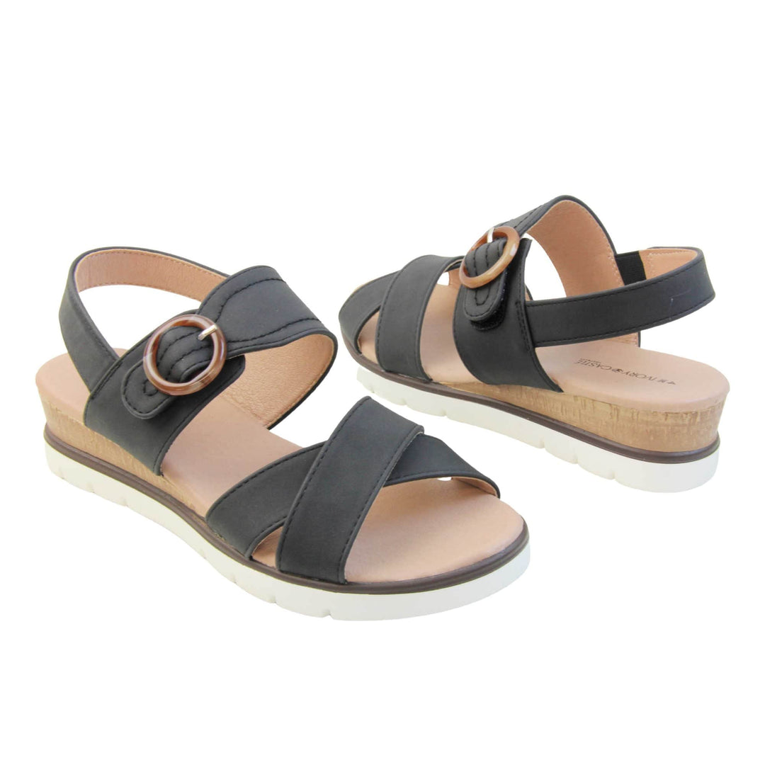Womens memory foam sandals. Classic womens strappy sandals with black textile straps. Dual toe straps that cross over each other. The ankle strap is touch fasten but has a brown buckle detail to look like a buckle fastening. Beige faux leather memory foam insoles. Small wedge heel in cork effect. White outsole with a black rim around the top. Both shoes about an inch apart at a slight angle facing top to tail.