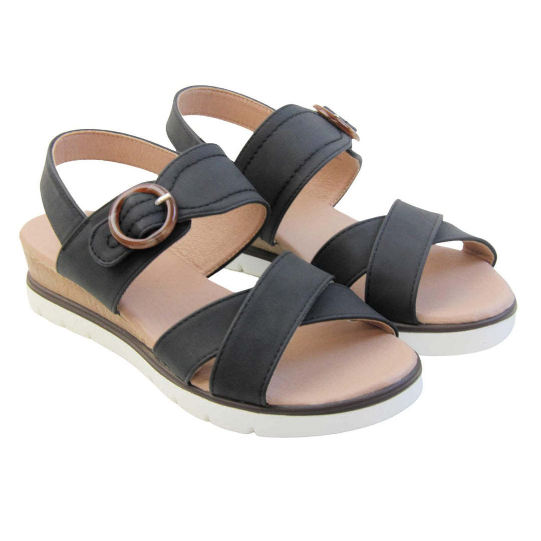 Womens memory foam sandals. Classic womens strappy sandals with black textile straps. Dual toe straps that cross over each other. The ankle strap is touch fasten but has a brown buckle detail to look like a buckle fastening. Beige faux leather memory foam insoles. Small wedge heel in cork effect. White outsole with a black rim around the top. Both shoes together from an angle