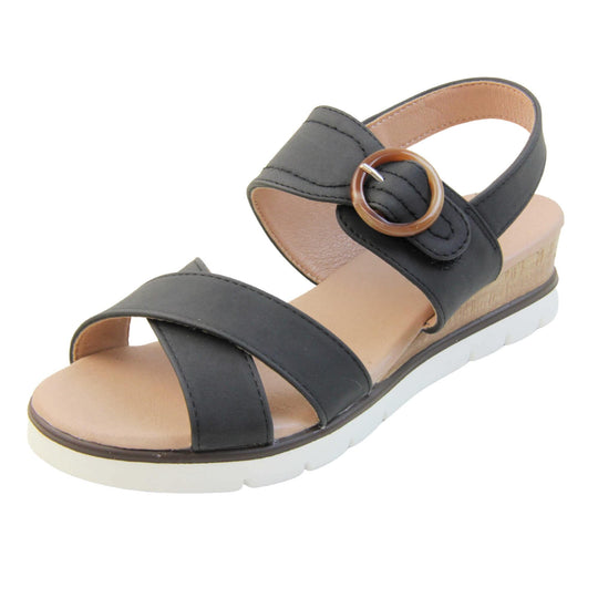 Womens memory foam sandals. Classic womens strappy sandals with black textile straps. Dual toe straps that cross over each other. The ankle strap is touch fasten but has a brown buckle detail to look like a buckle fastening. Beige faux leather memory foam insoles. Small wedge heel in cork effect. White outsole with a black rim around the top. Left foot at an angle.