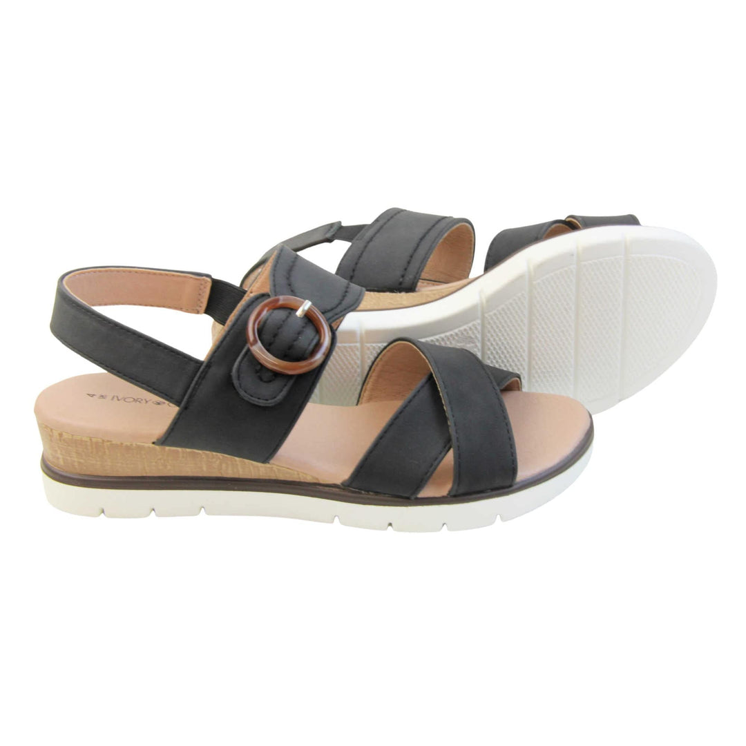 Womens memory foam sandals. Classic womens strappy sandals with black textile straps. Dual toe straps that cross over each other. The ankle strap is touch fasten but has a brown buckle detail to look like a buckle fastening. Beige faux leather memory foam insoles. Small wedge heel in cork effect. White outsole with a black rim around the top. Both feet from a side profile with left foot on its side behind the right to show the sole.