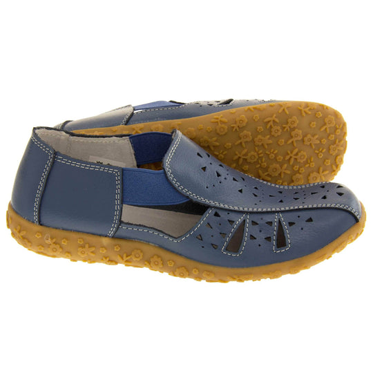 Womens navy sandals. Navy blue leather closed toe sandals with white stitched detailing. With small cut out details on the upper. Blue elasticated strips from tongue to ankle to allow more room for a better fit. Cream coloured leather insole and lining. Brown sole with heel having a slight platform with raised flower design for grip. Both feet from side profile with left foot on its side behind the right to show the sole.