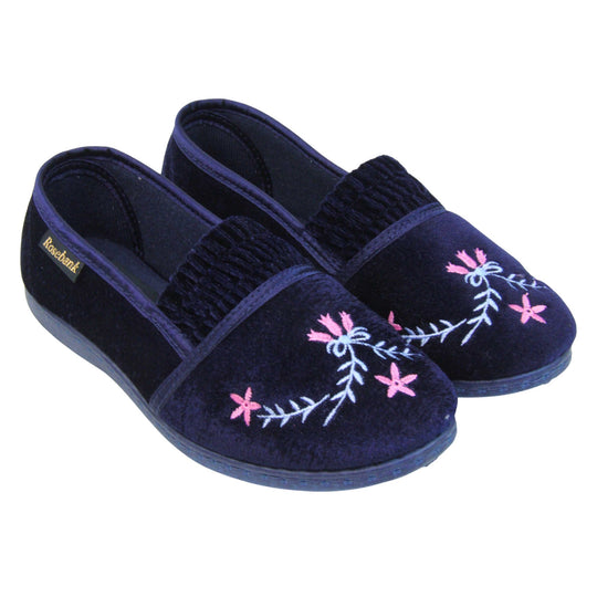 Womens navy slippers. Full back slippers in a loafer style. With navy blue velour uppers and a embroidered pale blue and pink flower detail. Ruched velour elasticated gusset. Navy textile lining and piping around the collar. Dark blue firm sole. Both feet together at an angle.