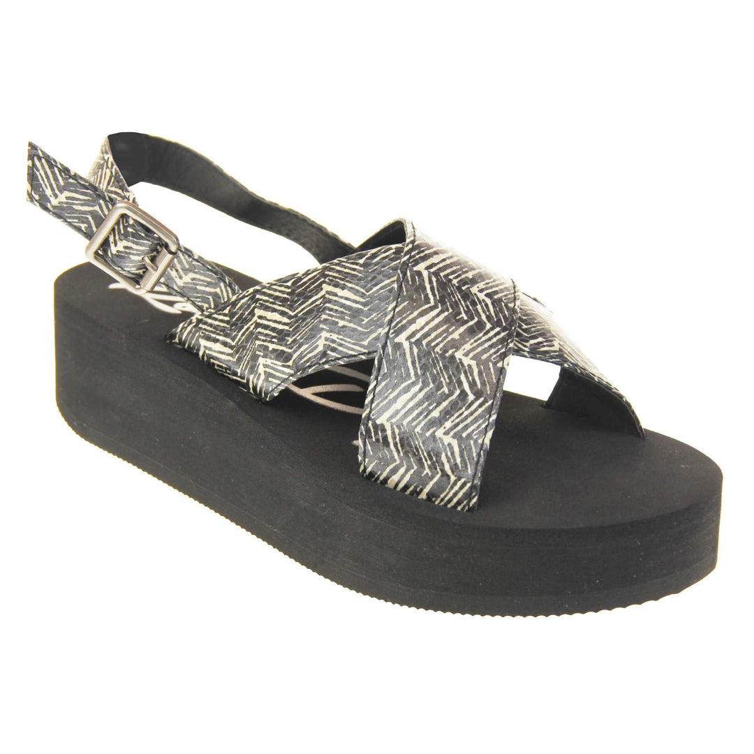 Womens platform wedge sandals - Black foam platform outsole with a black and cream upper with a zigzag design. Two straps crossed over the top of the foot and a strap around the back of the ankle. Silver buckle fastening to the outside of the ankle strap. Right foot at an angle.