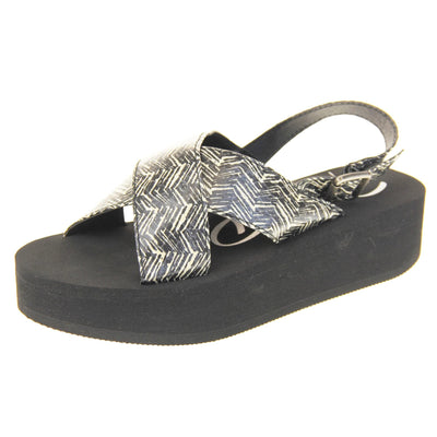 Womens platform wedge sandals - Black foam platform outsole with a black and cream upper with a zigzag design. Two straps crossed over the top of the foot and a strap around the back of the ankle. Silver buckle fastening to the outside of the ankle strap. Left foot at an angle.