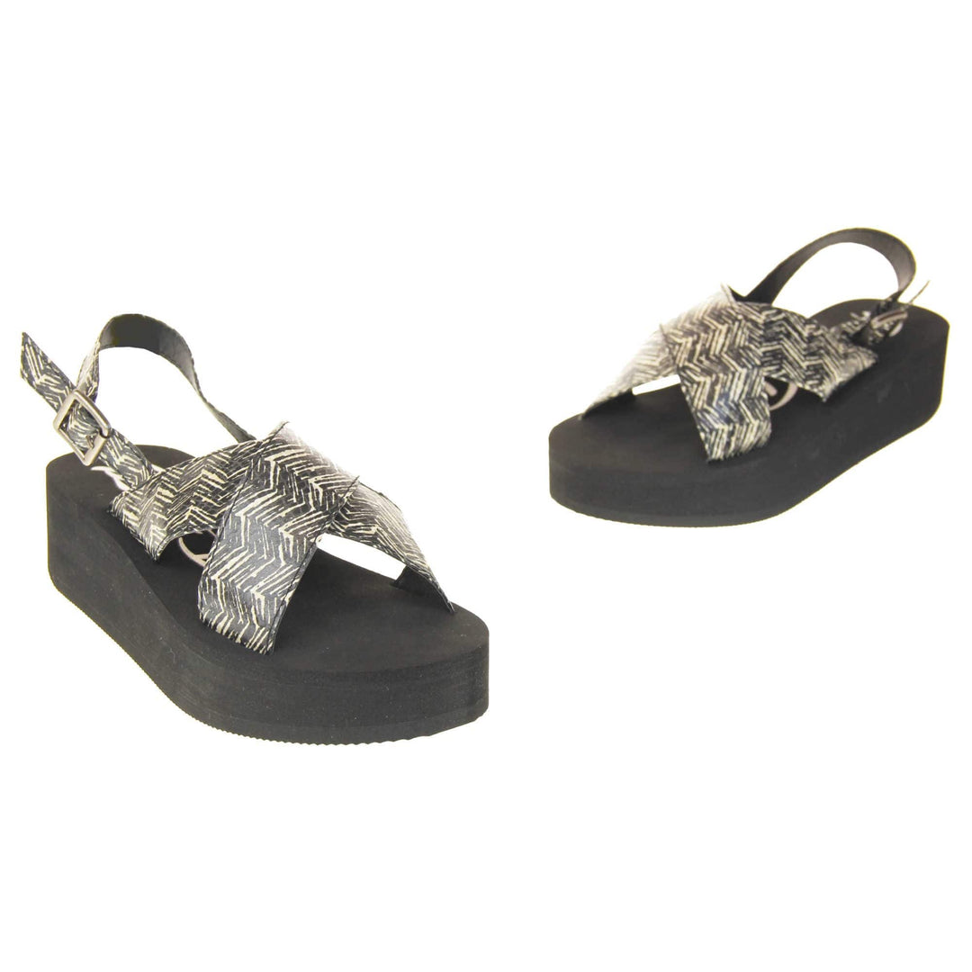 Womens platform wedge sandals - Black foam platform outsole with a black and cream upper with a zigzag design. Two straps crossed over the top of the foot and a strap around the back of the ankle. Silver buckle fastening to the outside of the ankle strap. Right foot side on. Both feet facing in a V shape with toes towards each other.