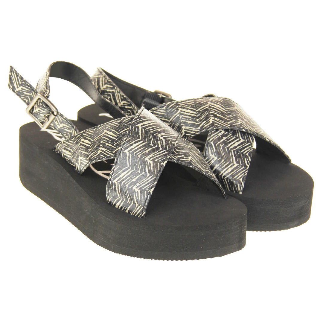 Womens platform wedge sandals - Black foam platform outsole with a black and cream upper with a zigzag design. Two straps crossed over the top of the foot and a strap around the back of the ankle. Silver buckle fastening to the outside of the ankle strap. Both feet at an angle.