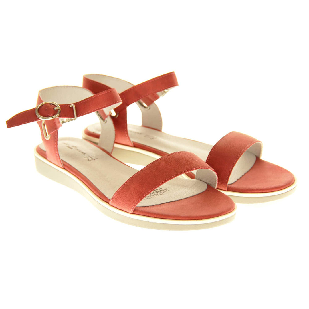 Womens red flat sandals. Classic womens strappy sandals with red faux leather straps around the ankle and over the toes. The ankle strap has a gold buckle fastening. Beige faux leather cushioned insoles. Very small wedge heel with beige outsole with a white rim around the top. Both shoes together from an angle