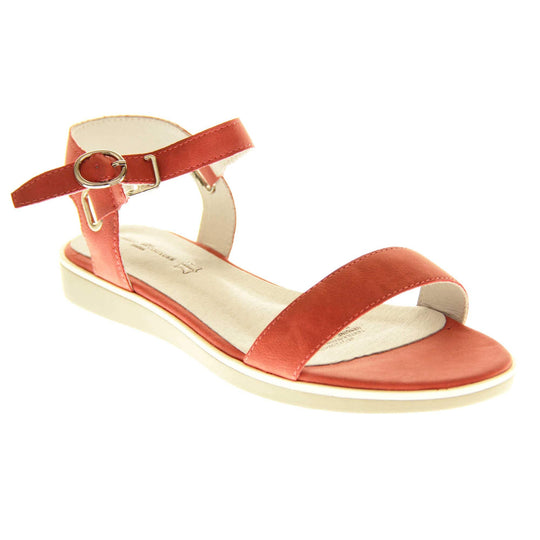 Womens red flat sandals. Classic womens strappy sandals with red faux leather straps around the ankle and over the toes. The ankle strap has a gold buckle fastening. Beige faux leather cushioned insoles. Very small wedge heel with beige outsole with a white rim around the top. Right foot at an angle.