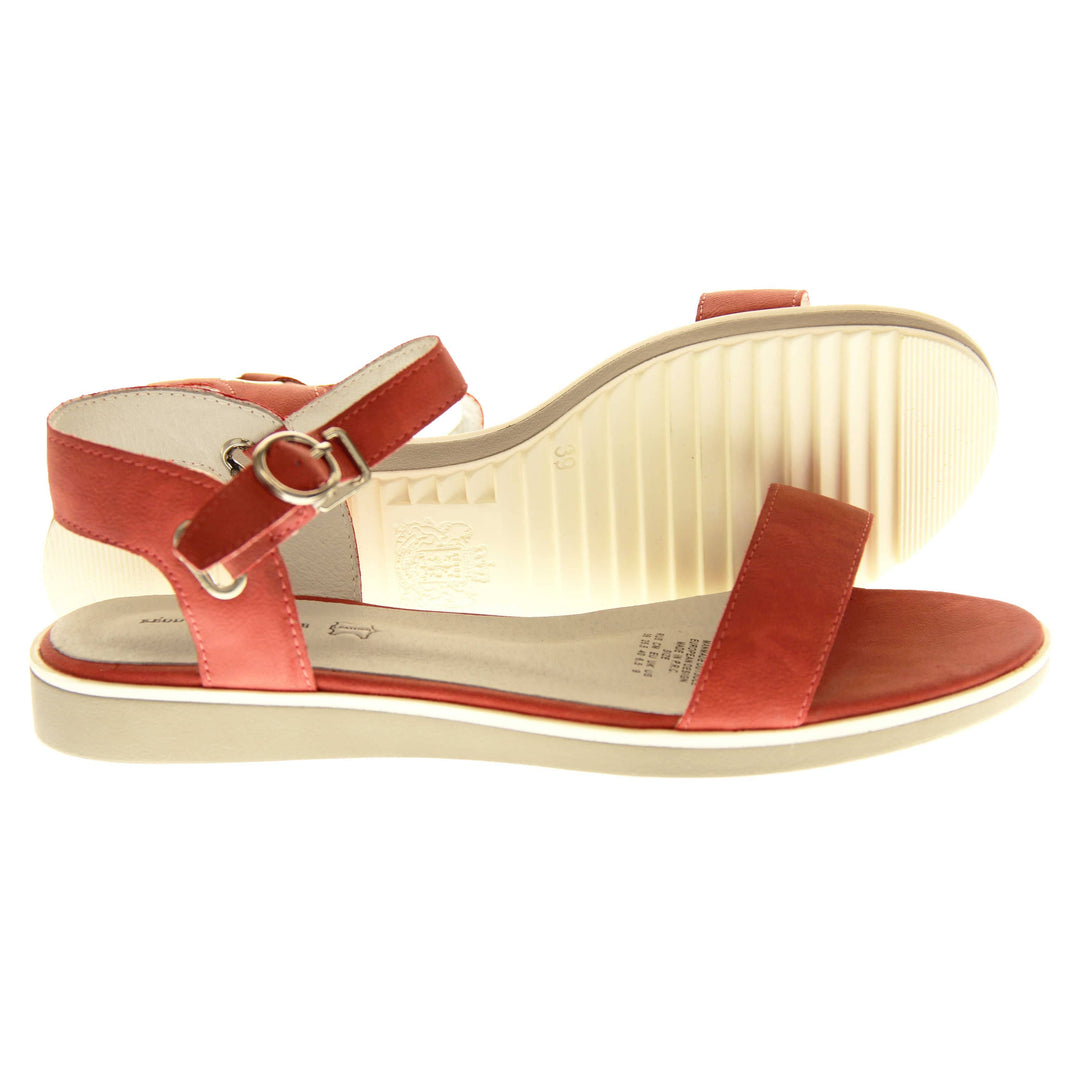 Womens red flat sandals. Classic womens strappy sandals with red faux leather straps around the ankle and over the toes. The ankle strap has a gold buckle fastening. Beige faux leather cushioned insoles. Very small wedge heel with beige outsole with a white rim around the top. Both feet from a side profile with left foot on its side behind the right to show the sole.