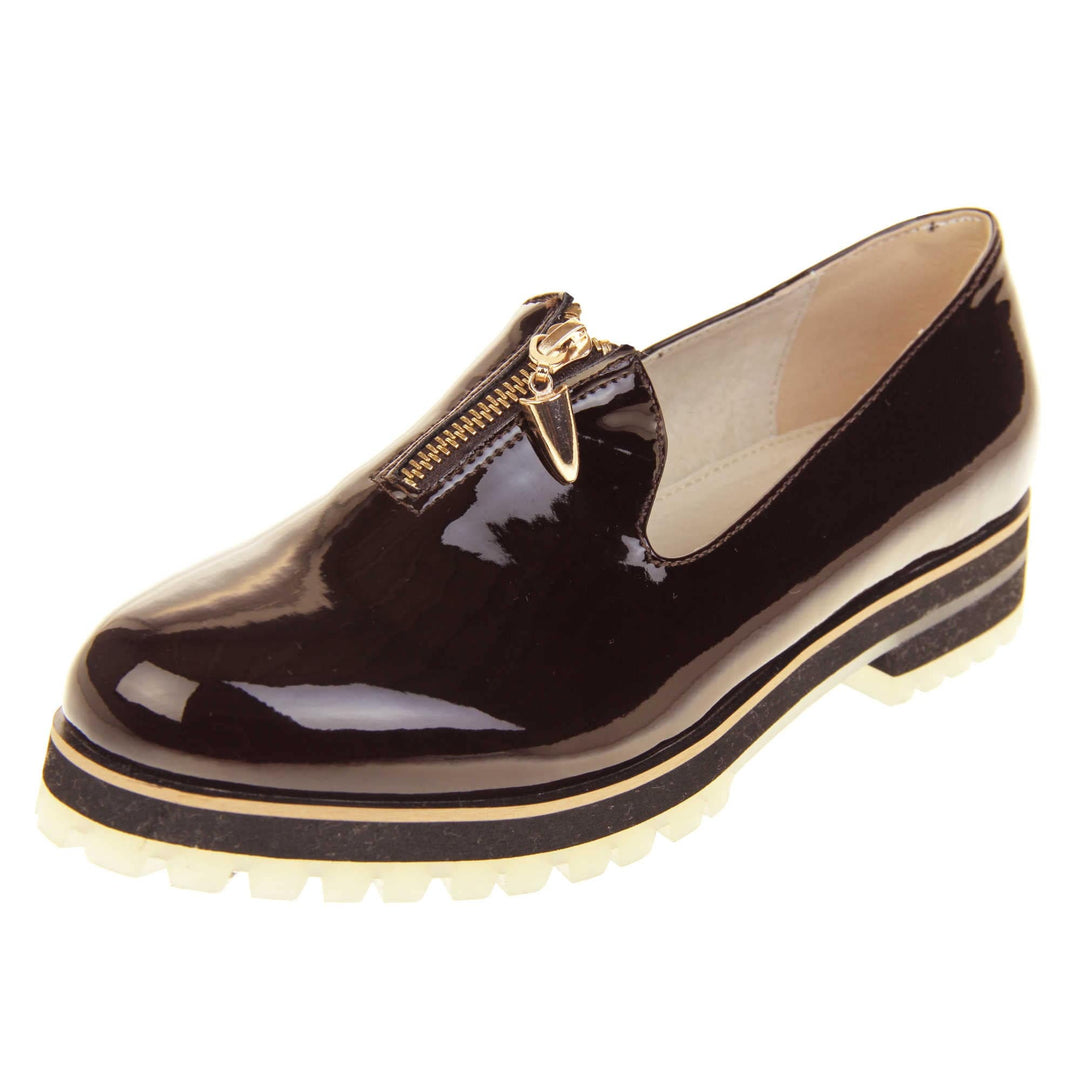 Womens red loafers. Loafer style shoes with dark burgundy patent uppers. Short gold zip detail to the top of the shoe. Black sole with cream base and small heel and beige leather lining. Left foot at an angle.