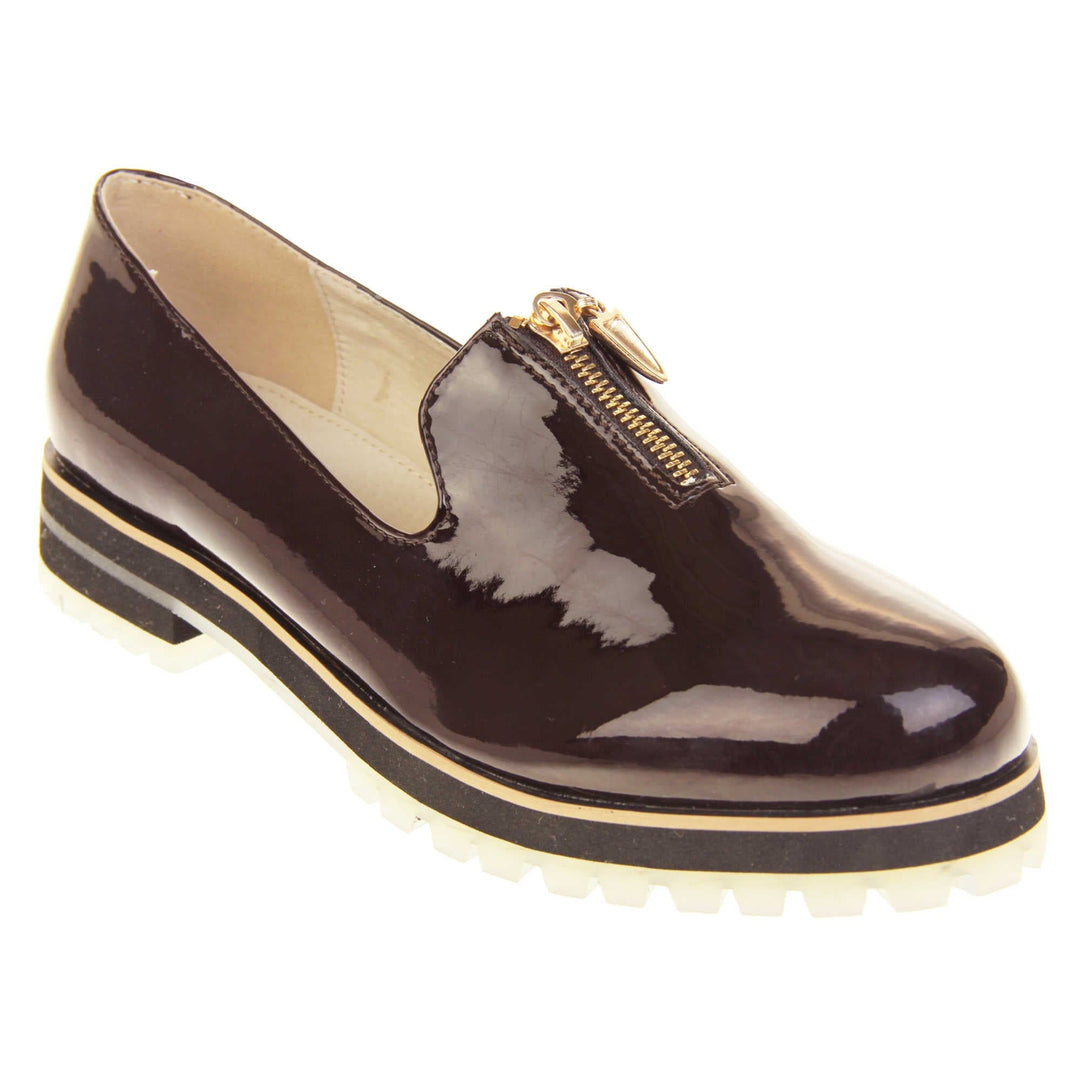 Womens red loafers. Loafer style shoes with dark burgundy patent uppers. Short gold zip detail to the top of the shoe. Black sole with cream base and small heel and beige leather lining. Right foot at an angle.