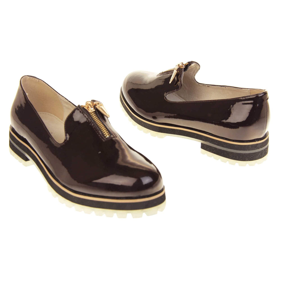 Womens red loafers. Loafer style shoes with dark burgundy patent uppers. Short gold zip detail to the top of the shoe. Black sole with cream base and small heel and beige leather lining. Both feet at an angle facing top to tail.