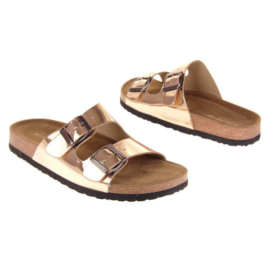 Womens rose gold sandals. Ladies dual strap slip on sandals. With a metallic rose gold synthetic leather upper with a pewter buckle on each strap. Brown faux suede insole with a moulded footbed. Cork effect outsole with black base with grip to the bottom. Both feet at an angle facing top to tail.