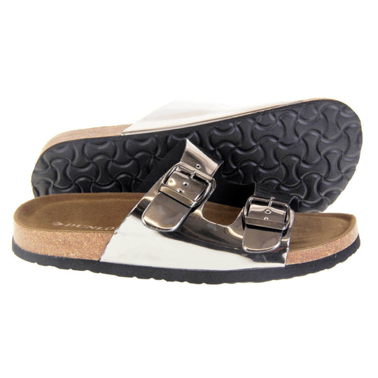 Womens silver sandals. Ladies dual strap slip on sandals. With a metallic pewter synthetic leather upper and pewter buckle on each strap. Brown faux suede insole with a moulded footbed. Cork effect outsole with black base with grip to the bottom. Both feet from a side profile with the left foot on its side behind the the right foot to show the sole.