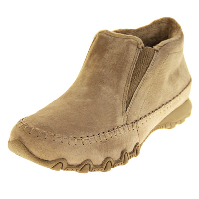 Womens Skechers boots. Sand coloured suede uppers in an ankle boot style. With brown elasticated panels by the tongue. Brown chenille lining. Brown sole with grip the bottom. Left foot at an angle.
