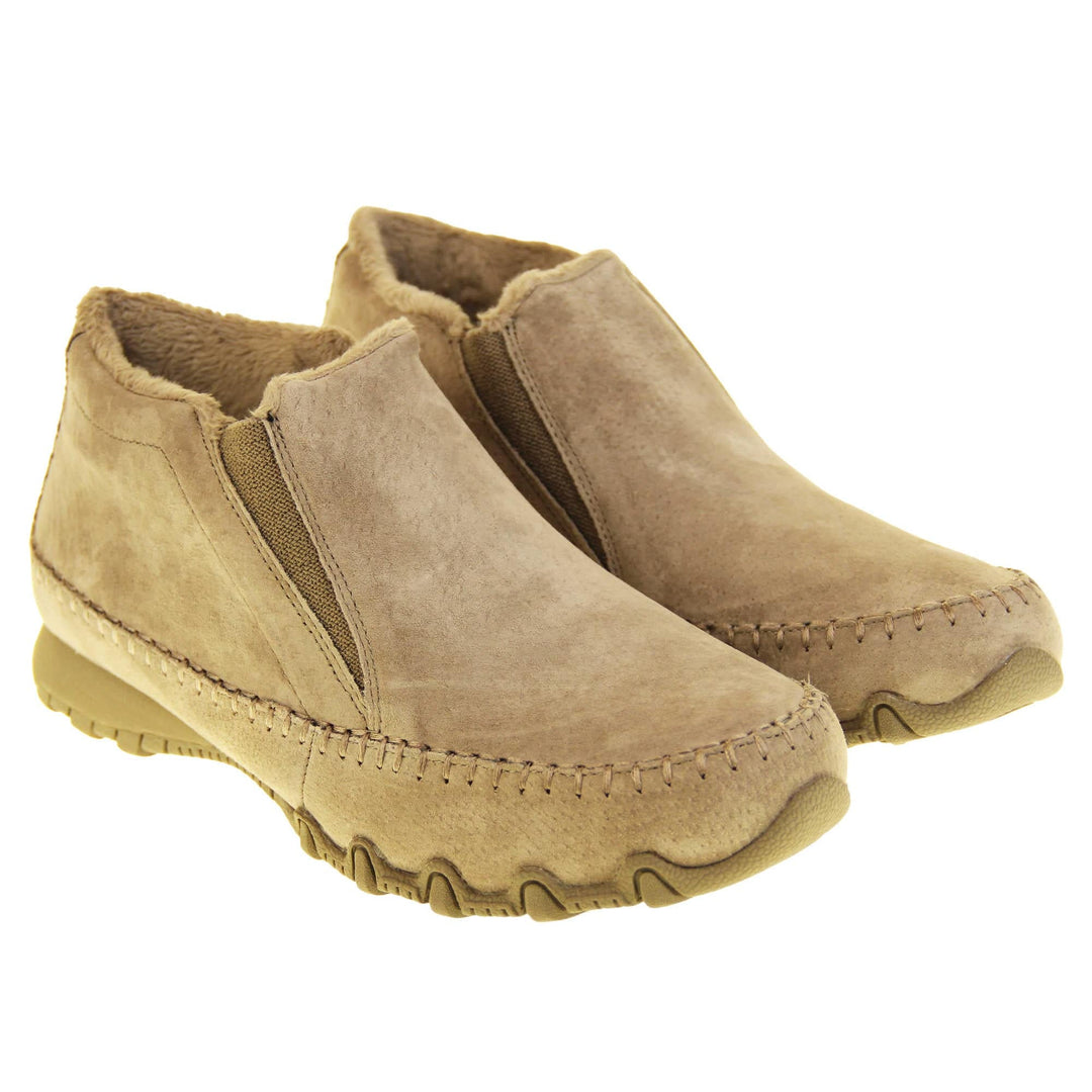 Womens Skechers boots. Sand coloured suede uppers in an ankle boot style. With brown elasticated panels by the tongue. Brown chenille lining. Brown sole with grip the bottom. Both feet at an angle with cuff raised.