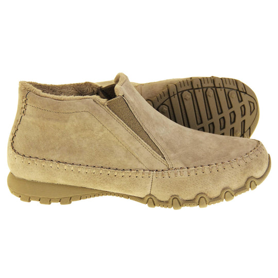 Womens Skechers boots. Sand coloured suede uppers in an ankle boot style. With brown elasticated panels by the tongue. Brown chenille lining. Brown sole with grip the bottom. Both feet from a side profile with the left foot on its side to show the sole.
