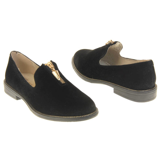 Womens smart loafers. Loafer style shoes with black faux suede uppers. Short gold zip detail to the top of the shoe. Gold stud detail around the rim of the sole. Black sole with very small heel and beige leather lining. Left foot at an angle. Both feet at an angle facing top to tail.