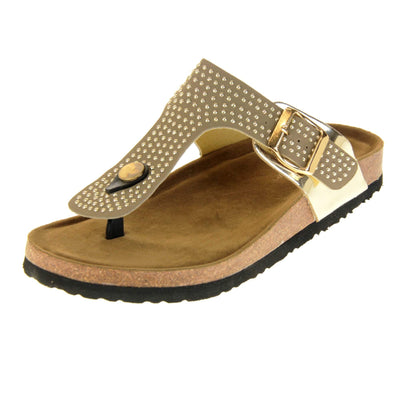 Womens studded sandals. Taupe faux leather strap covered in gold studs. With black toe post to the front and gold buckle to the outside. Metallic gold strap to the side meeting at the buckle. Soft tan faux suede footbed with cork effect outsole and black sole. Left foot at an angle.