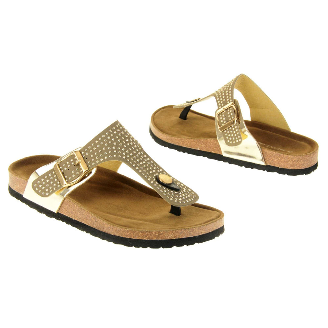 Womens studded sandals. Taupe faux leather strap covered in gold studs. With black toe post to the front and gold buckle to the outside. Metallic gold strap to the side meeting at the buckle. Soft tan faux suede footbed with cork effect outsole and black sole. Both feet at an angle facing top to tail.