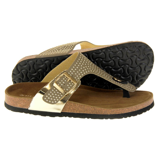 Womens studded sandals. Taupe faux leather strap covered in gold studs. With black toe post to the front and gold buckle to the outside. Metallic gold strap to the side meeting at the buckle. Soft tan faux suede footbed with cork effect outsole and black sole. Both feet from a side profile with the left foot on its side behind the the right foot to show the sole.
