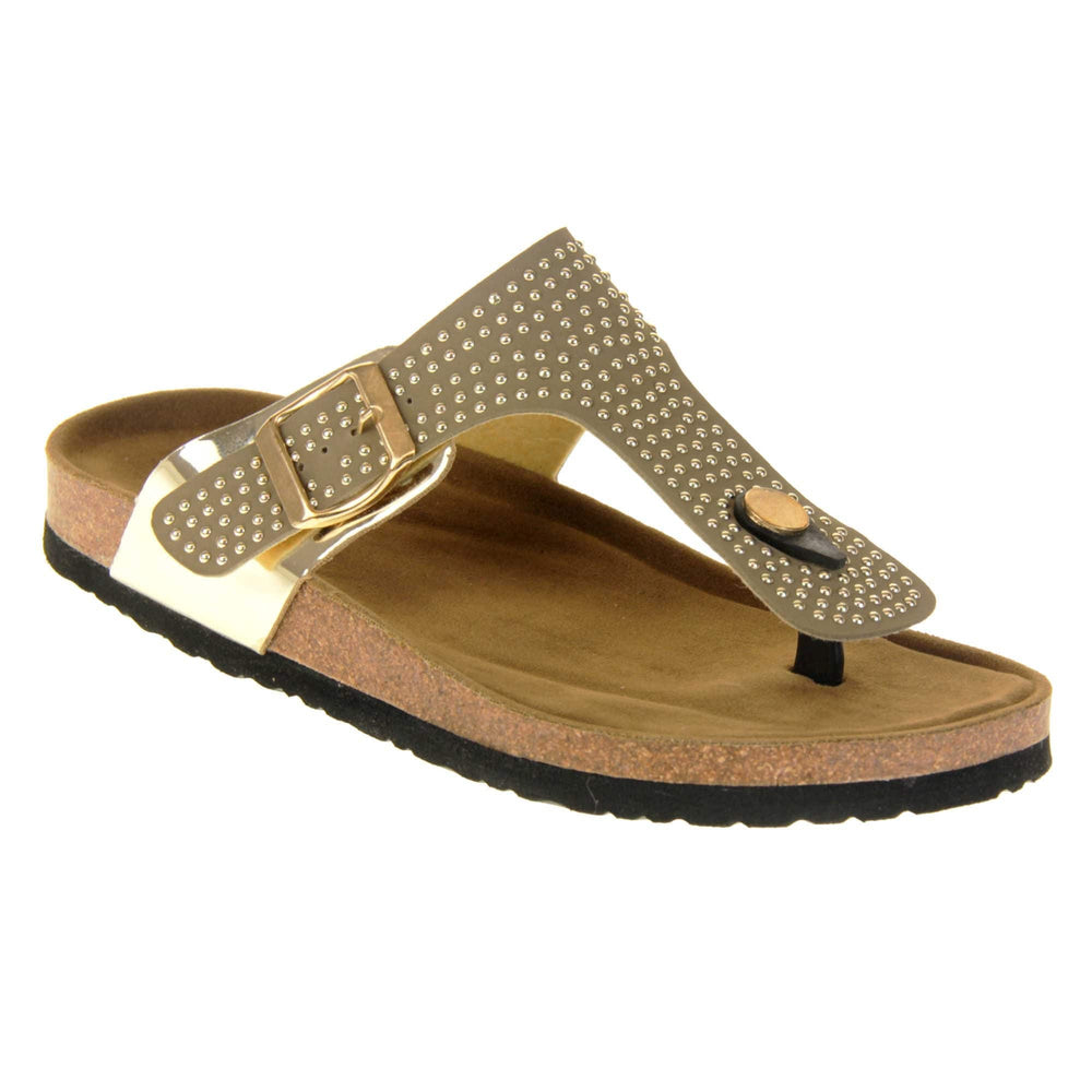Womens studded sandals. Taupe faux leather strap covered in gold studs. With black toe post to the front and gold buckle to the outside. Metallic gold strap to the side meeting at the buckle. Soft tan faux suede footbed with cork effect outsole and black sole. Right foot at an angle.