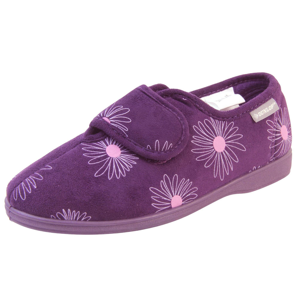 Womens washable slippers. Ladies full back slipper. Purple upper with white daisy design and bright pink for the middle of the flowers. Touch fasten strap over the top of the foot to adjust the fit. Matching purple textile lining and firm purple sole. Left foot at an angle.