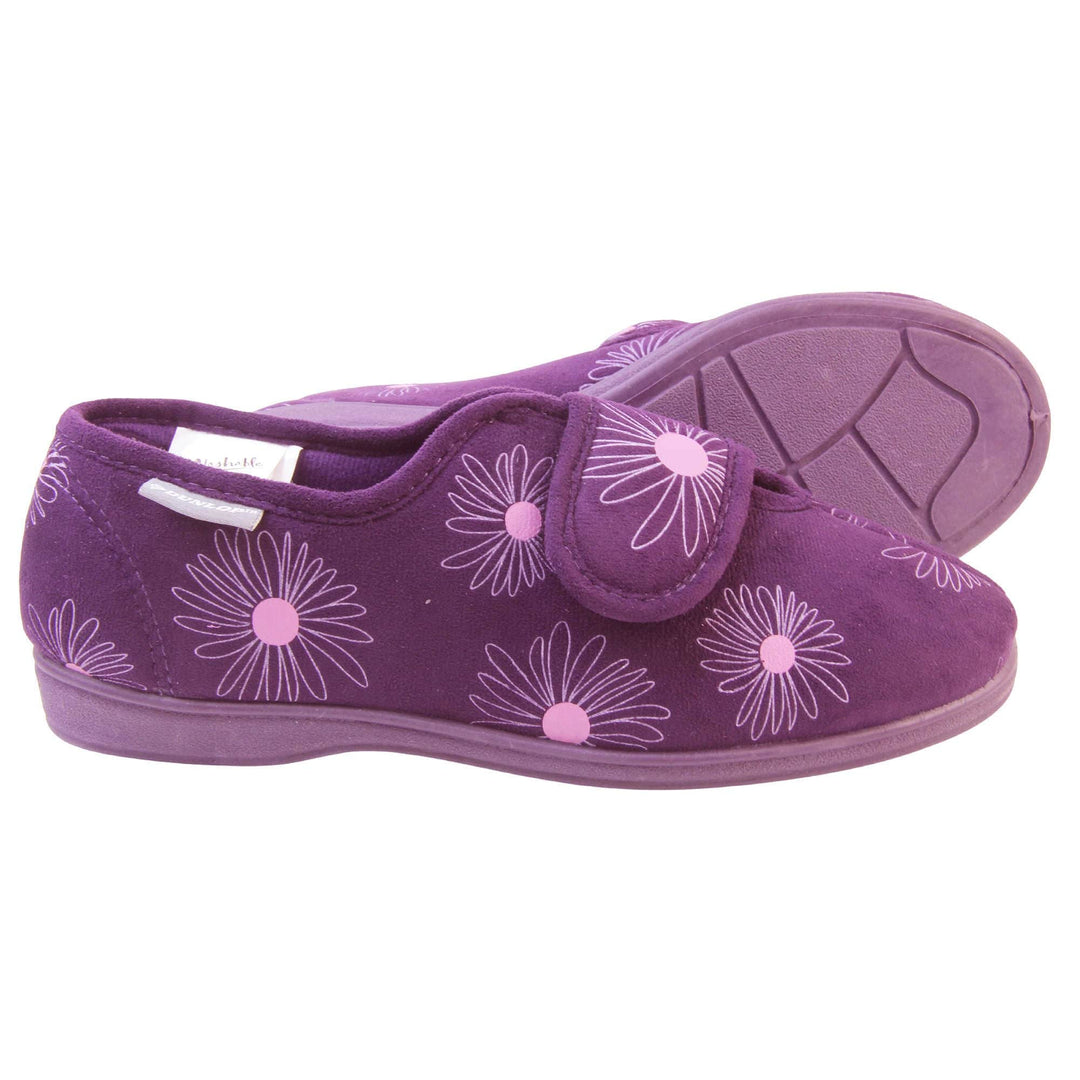 Womens washable slippers. Ladies full back slipper. Purple upper with white daisy design and bright pink for the middle of the flowers. Touch fasten strap over the top of the foot to adjust the fit. Matching purple textile lining and firm purple sole. Both feet from a side profile with the left foot on its side behind the the right foot to show the sole.