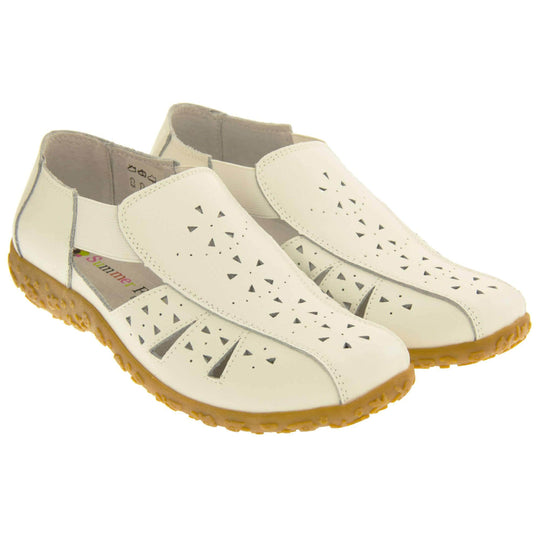 Womens white sandals. White leather closed toe sandals with white stitched detailing. With small cut out details on the upper. White elasticated strips from tongue to ankle to allow more room for a better fit. Cream coloured leather insole and lining. Brown sole with heel having a slight platform with raised flower design for grip. Both feet together from an angle.